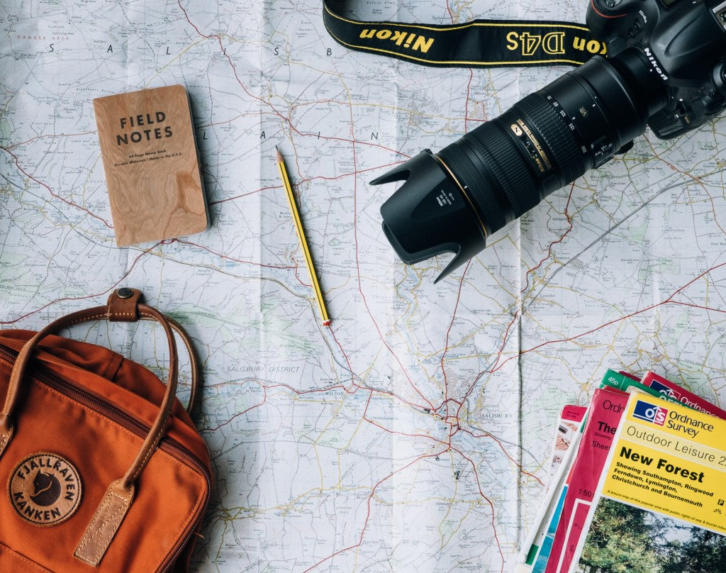 Macchina fotografica, taccuino, guide e borsa su una carta geografica.