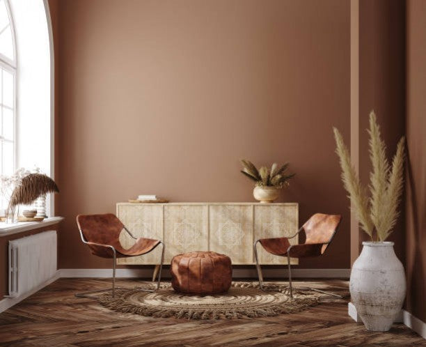 Soggiorno nei toni marroni con tavolo, sedute e parete color terracotta.