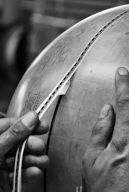 Applicazione manuale dei fusi cartografici sulla sfera di un mappamondo.